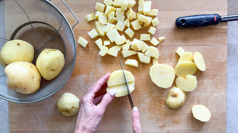 mains coupant des pommes de terre en cubes