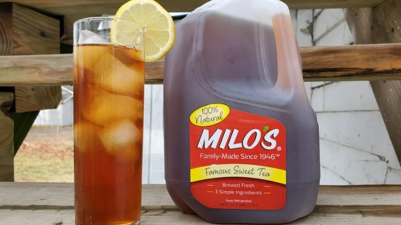 Une grande bouteille de Milo's Famous Sweet Tea à côté d'un verre de thé glacé avec une tranche de citron dedans.