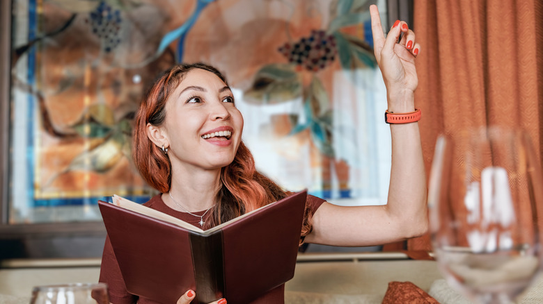 personne tenant un menu dans un restaurant et signalant au serveur