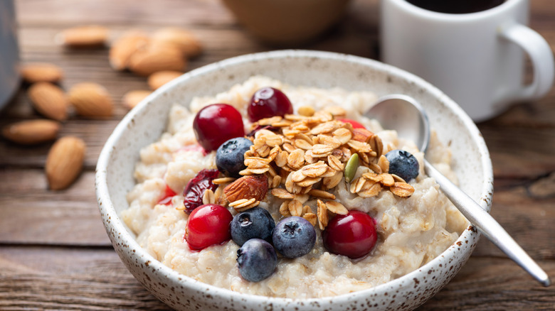 Bol de porridge aux flocons d'avoine avec baies, garniture granola croquante, tasse de café noir sur fond de table en bois rustique, vue rapprochée.