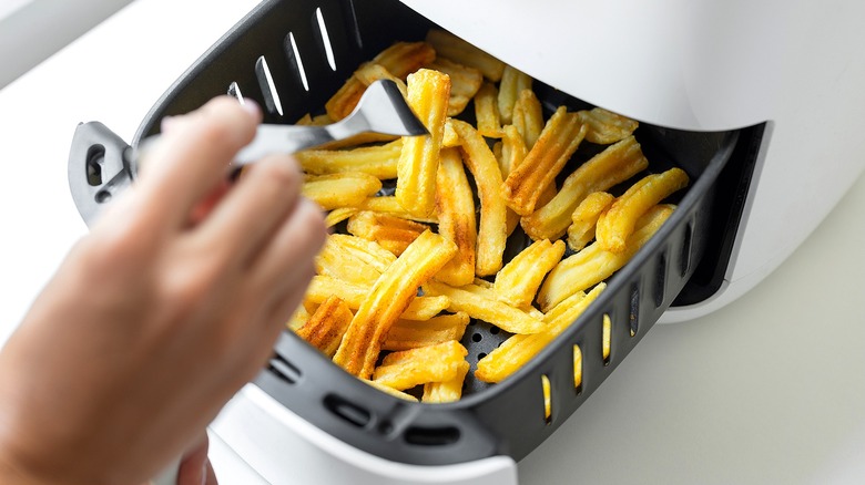 Retirer à la main une frite avec une fourchette en métal d'un panier de friteuse à air