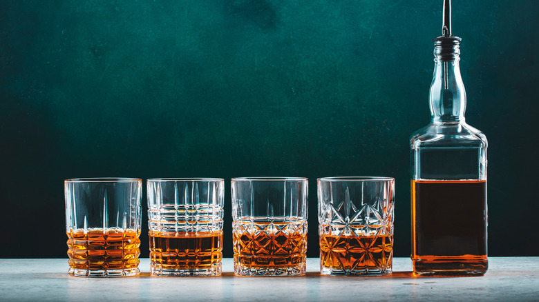 Une rangée de verres de scotch à côté d’une seule bouteille.