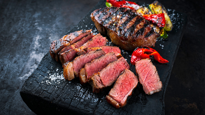 Bœuf Wagyu cuit aux légumes sur une plaque de bois carbonisé.