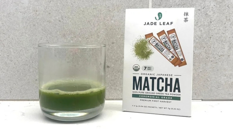 Paquet de Matcha Feuille de Jade à côté d'un petit verre de matcha mélangé à de l'eau
