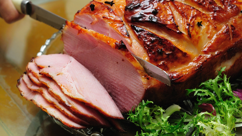 Un couteau à découper tranchant un jambon fumé sur un plateau en verre.