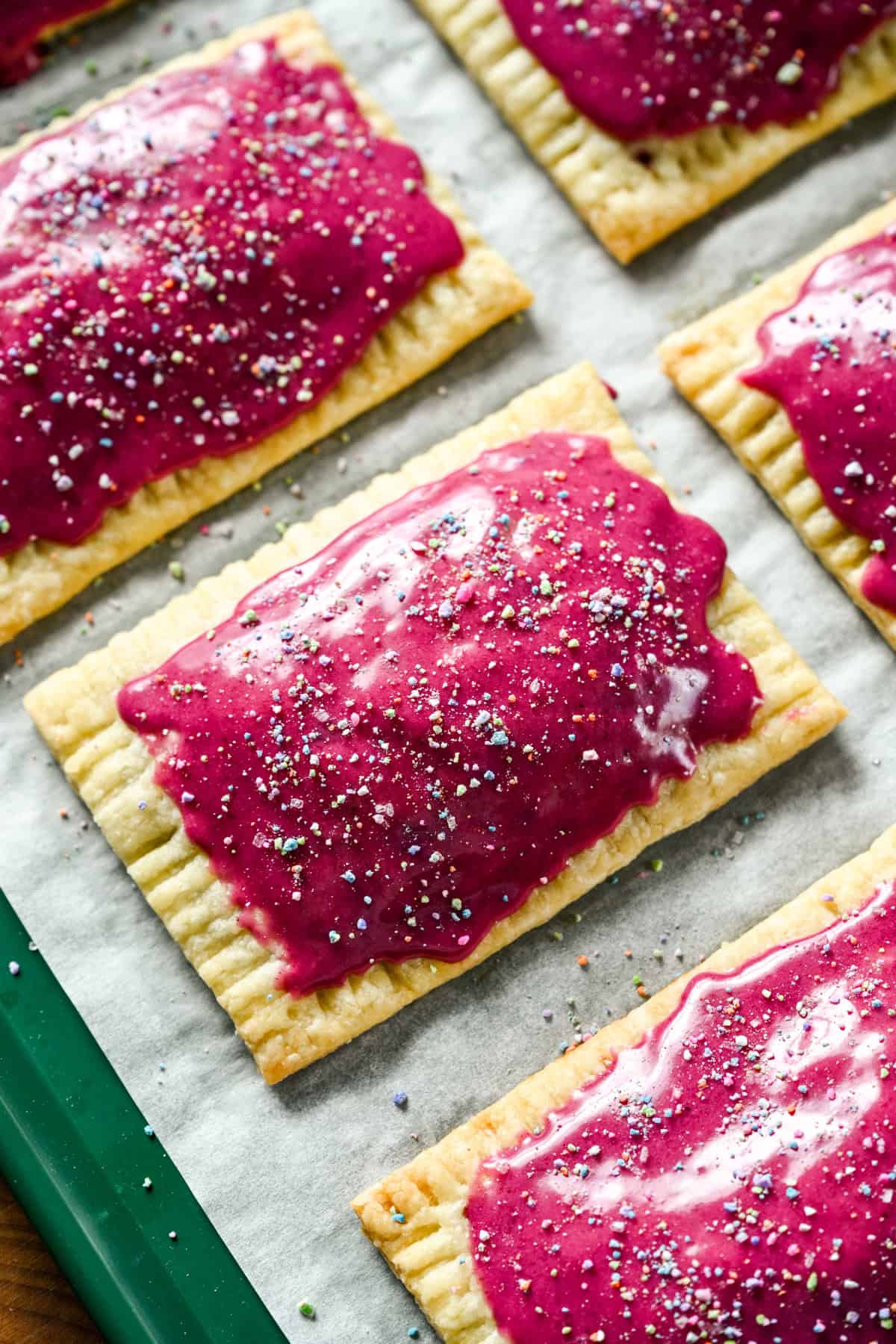 vue rapprochée des tartelettes pop aux bleuets faites maison avec un glaçage rose vif et des pépites sur une plaque à pâtisserie.