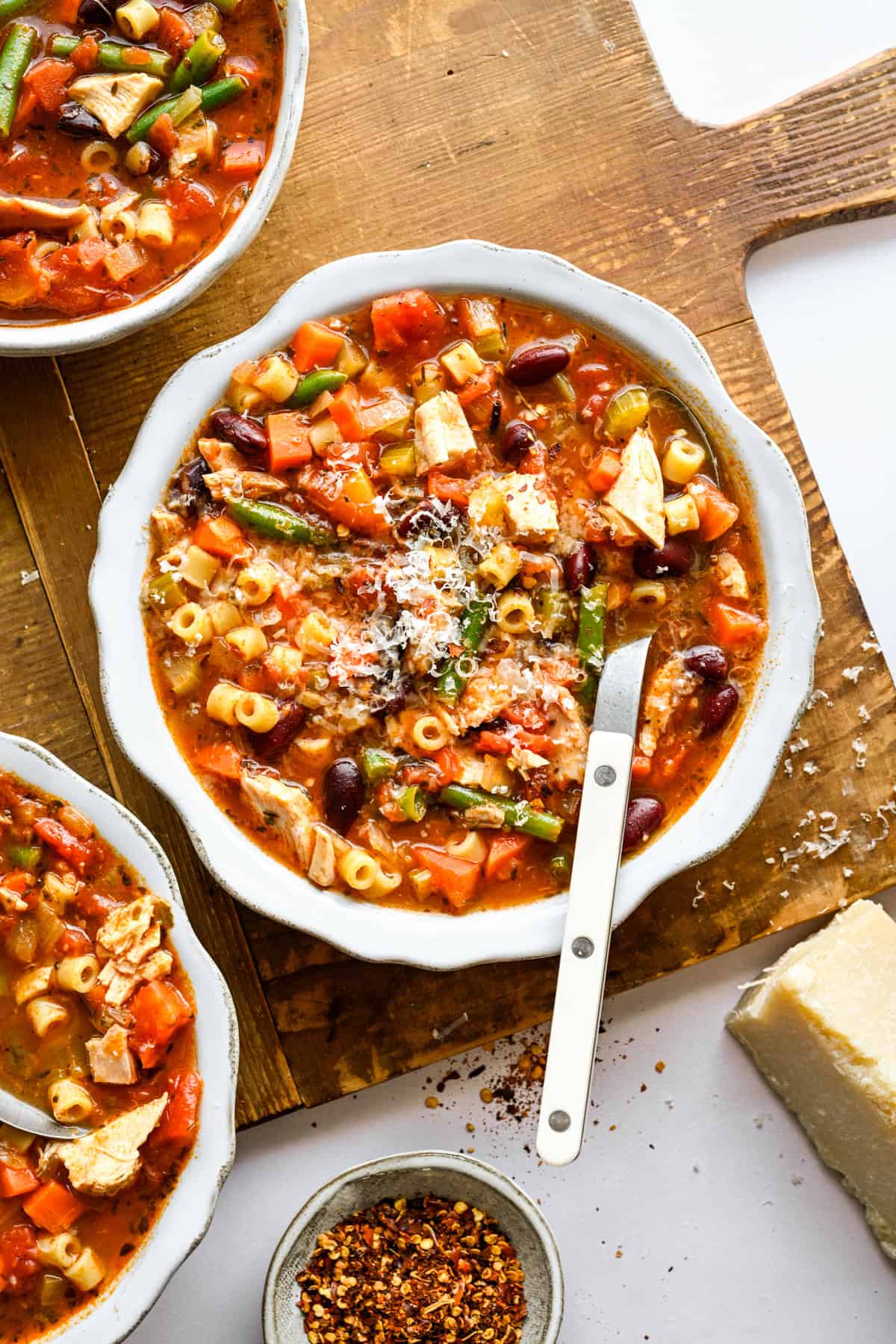Soupe minestrone au poulet avec une cuillère à soupe, garnie de parmesan frais.