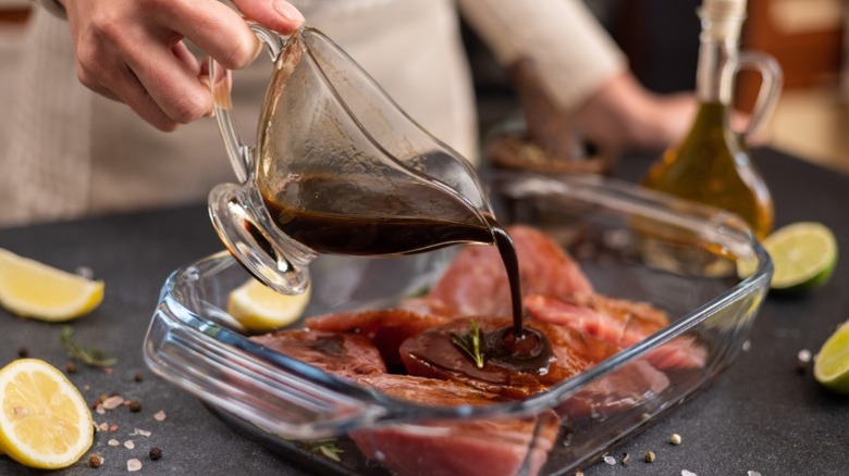 Un chef verse une marinade au whisky sur des morceaux de steak dans un plat allant au four.