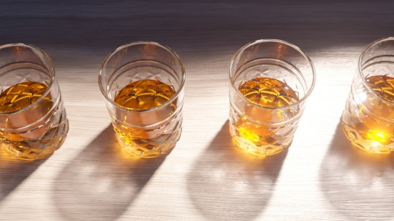 Verres de whisky versés proprement alignés sur une surface en bois avec la lumière du soleil qui brille sur eux.