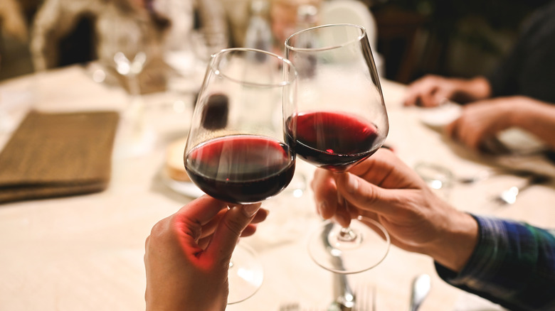 On voit des mains en train de trinquer avec du vin rouge à une table de restaurant.