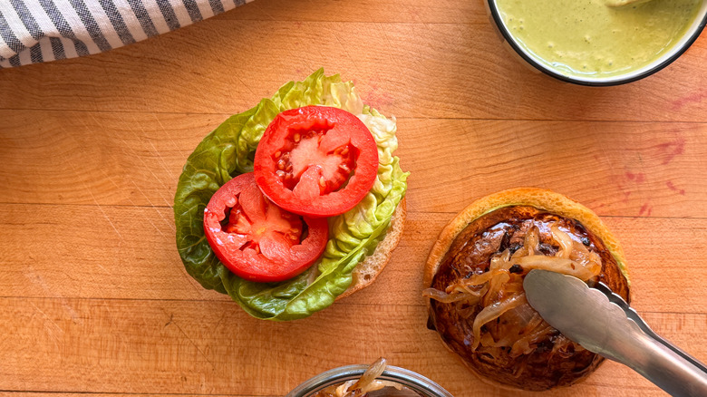 Burger ouvert avec tomates, laitue et pinces plaçant des oignons