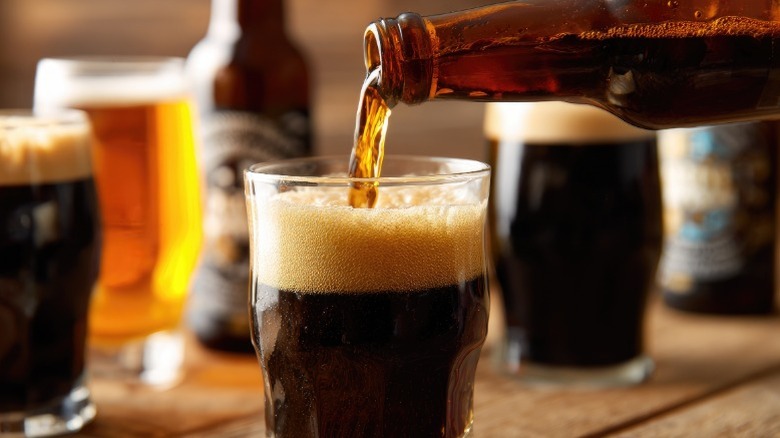 Une bière brune versée d'une bouteille dans un verre avec différents styles de bière assis dans des verres derrière.