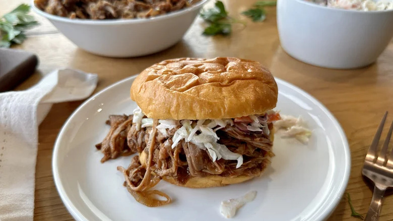 Sandwich au porc effiloché avec salade de chou sur une assiette blanche.