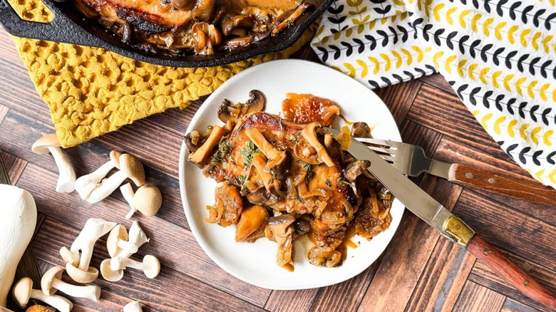 Une portion de côtelettes de porc recouvertes de champignons sur une assiette blanche avec fourchette et couteau.