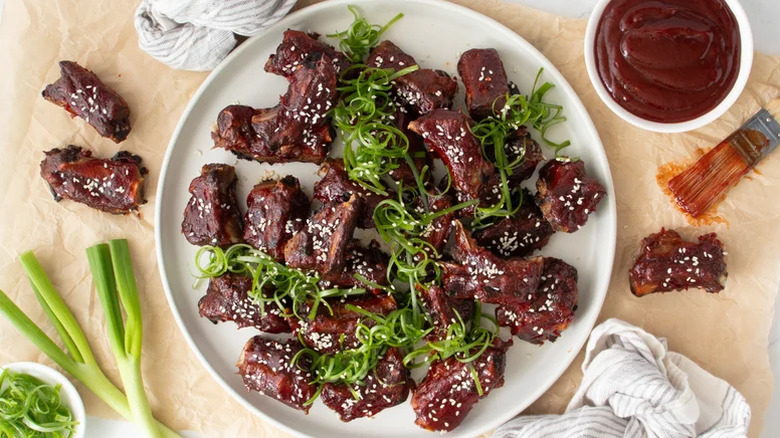 Riblets de porc sur une assiette blanche garnie de graines de sésame et d'oignons verts.
