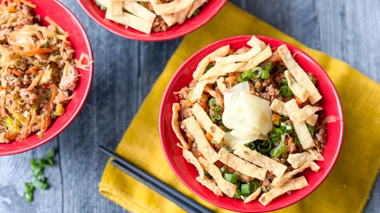 Trois bols de mélange de nems au porc garnis d'oignons verts, de gingembre et de lanières de wontons frits croustillants.