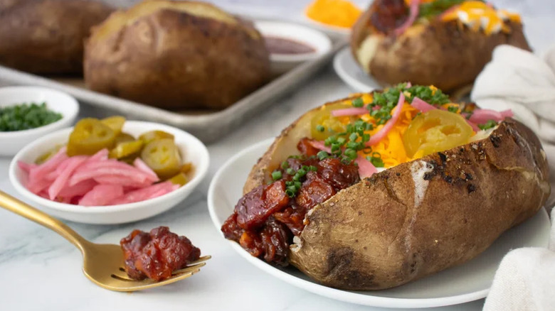 Pommes de terre au four sur une assiette avec diverses garnitures comme de la poitrine de porc, du fromage, de la ciboulette, des jalapeños et des oignons rouges marinés.