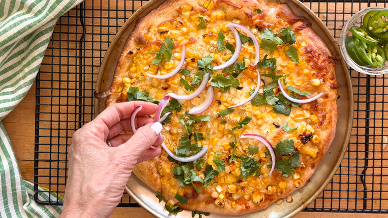 main ajoutant des oignons à la pizza