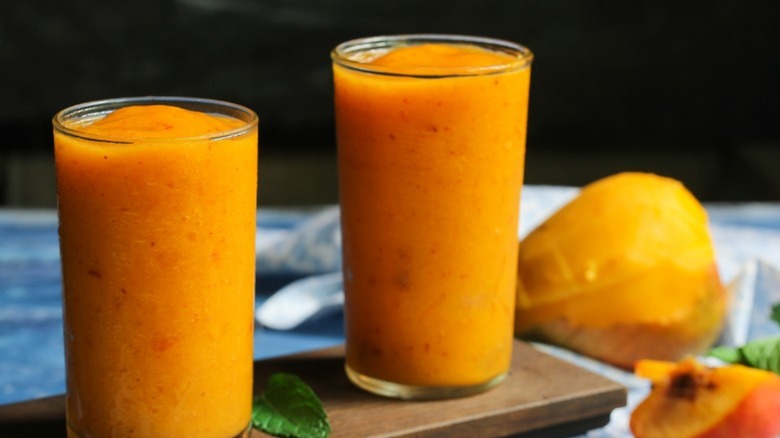 Deux verres de cocktails glacés fraîchement préparés avec de la mangue coupée et d'autres fruits en accompagnement.
