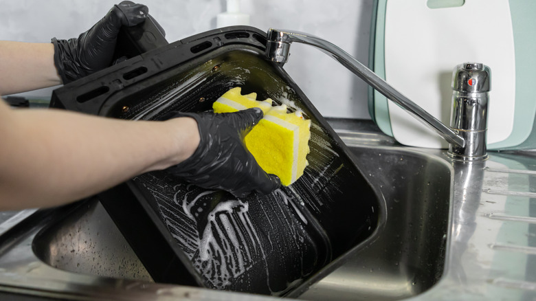 Une personne nettoyant le panier d'une friteuse à air avec une éponge et du savon.