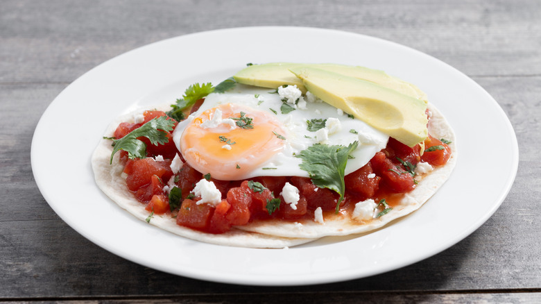 huevos rancheros sur une plaque blanche sur une table en bois