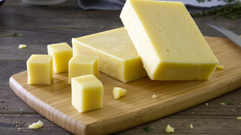 Les cubes et blocs de fromage sont disposés sur une planche à découper.