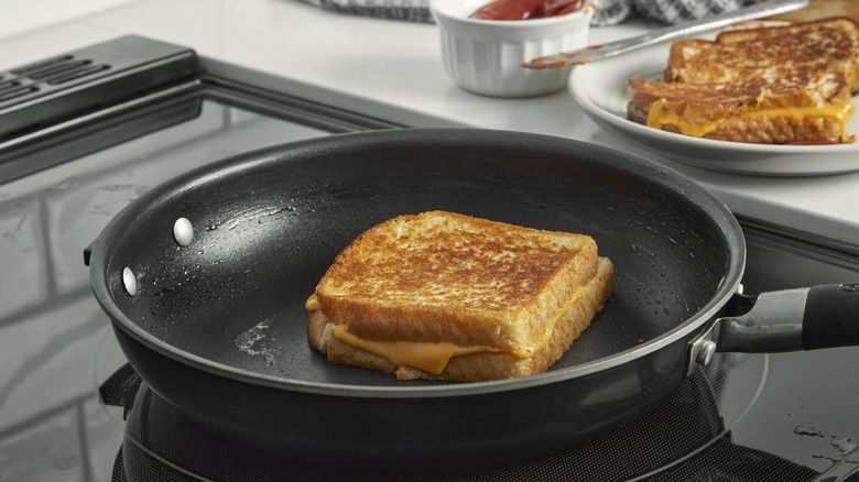 Le fromage grillé cuit dans une poêle sur une cuisinière avec d'autres sandwichs placés à proximité.