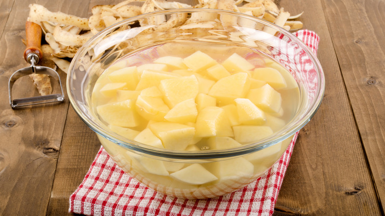pommes de terre coupées en dés dans un bol en verre avec de l'eau pour enlever la fécule de pomme de terre