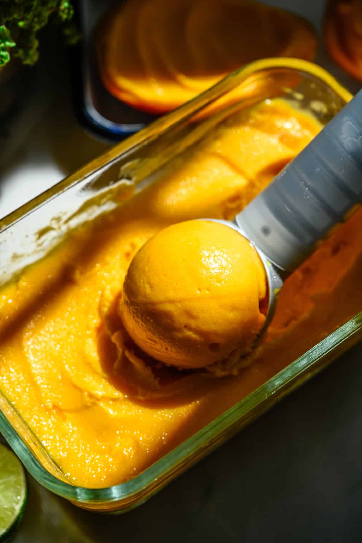 Vue rapprochée d'une boule de sorbet à la mangue posée dans un récipient de sorbet.