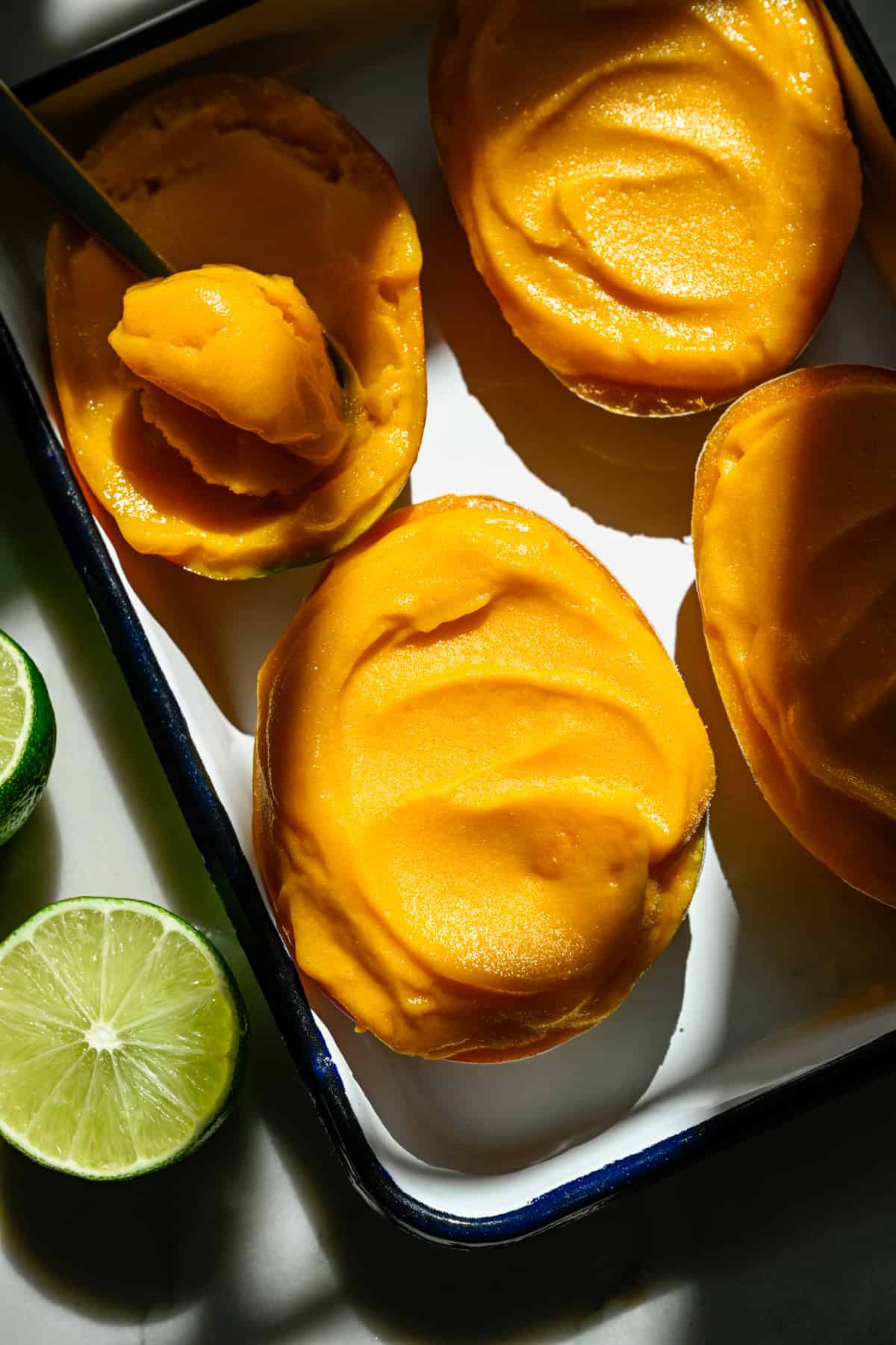 Vue aérienne d'un sorbet à la mangue dans une moitié de mangue sur une plaque avec quelques autres.