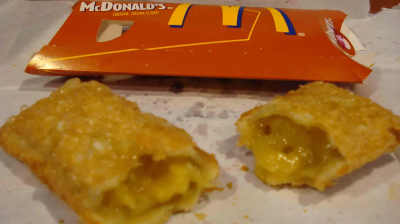 Une tarte aux pommes frites de McDonald's, ouverte pour révéler la garniture, repose sur un revêtement en papier sur une table à côté de sa pochette d'emballage en carton rouge.