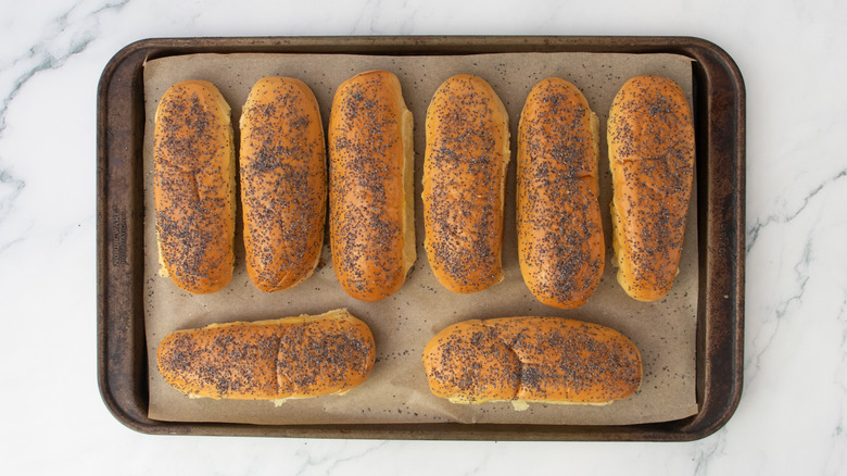 Petits pains à hot dog saupoudrés de graines de pavot sur une grande plaque à pâtisserie