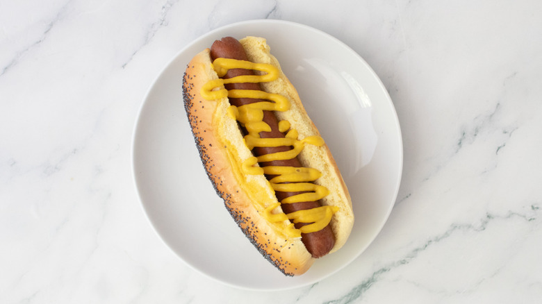 Hot dog dans un petit pain, arrosé de moutarde sur une assiette blanche