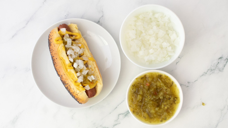 Hot-dog dans un petit pain, arrosé de moutarde et garni d'oignons et de relish.