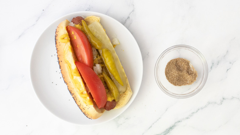 Hot-dog dans un petit pain garni d'oignons, de relish, de pointes de cornichon, de quartiers de tomates, de poivrons et de sel de céleri