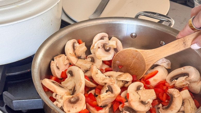 main en remuant les champignons et les poivrons