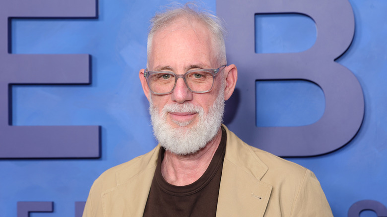 L'acteur Brian Koppelman porte des lunettes devant un mur bleu.