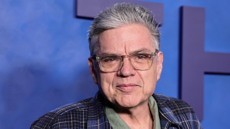 L'acteur Oliver Platt se tient devant un mur bleu.