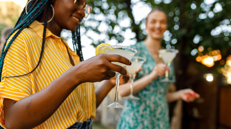 Deux jeunes femmes tenant des margaritas lors d'une fête en plein air l'après-midi.