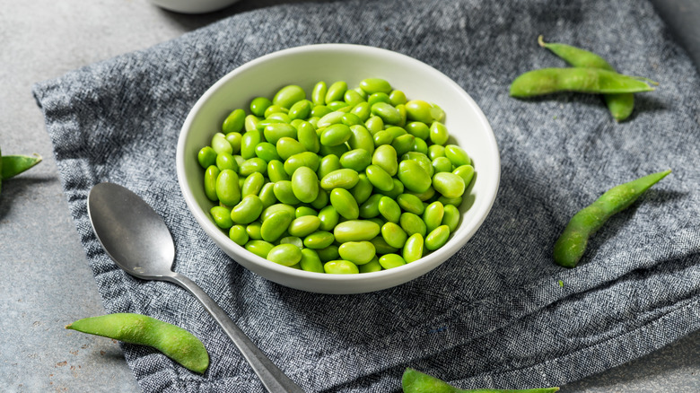 un bol d'edamame sur une serviette en tissu gris à côté d'une cuillère