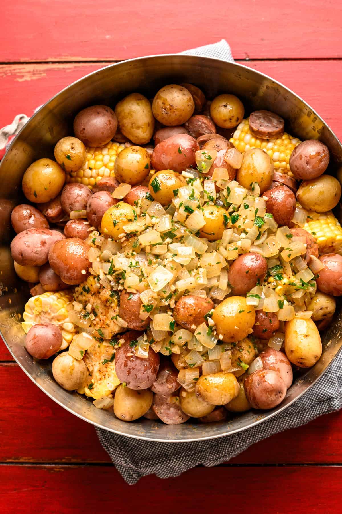 Crevettes, maïs, pommes de terre et saucisses dans un grand bol avec une sauce au beurre de vieux laurier et à l'ail versée sur le dessus avant de mélanger.