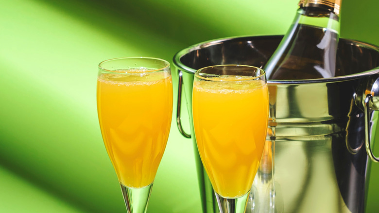 Deux cocktails mangue mimosa avec une bouteille de champagne reposant dans un seau en arrière-plan