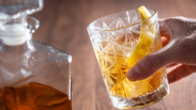 Une main tenant un cocktail d'ongles rouillés garni d'un zeste de citron