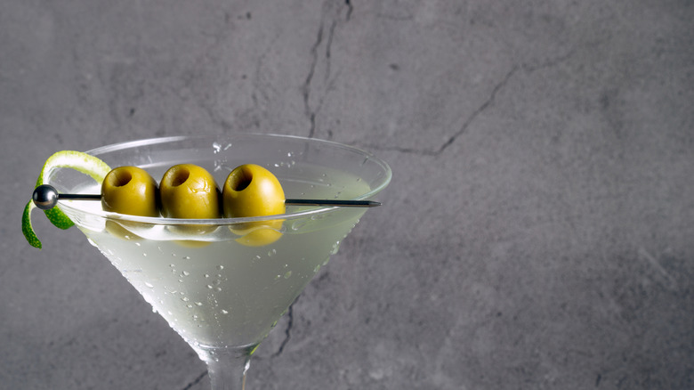 Un gros plan d'un cocktail martini dans un verre à martini avec trois olives et un zeste de citron vert