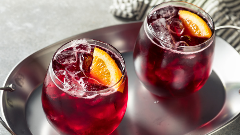 Deux spritzers à vin rouge dans des verres à vin sans pied sur un plateau argenté garni de quartiers d'orange