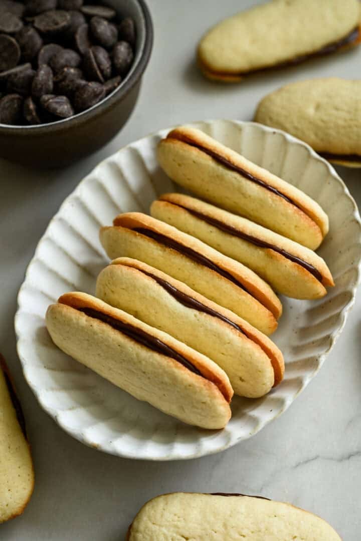 Vue à 45 degrés d'une pile de biscuits milanais faits maison dans un bol ovale blanc.