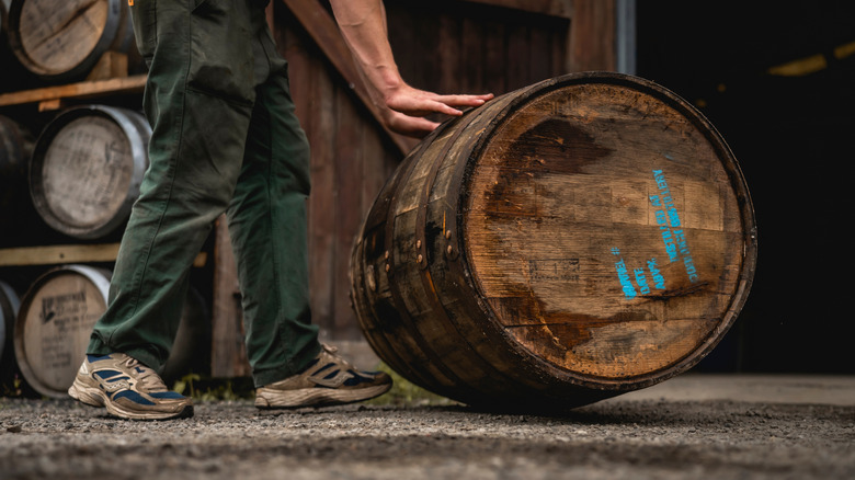 Ouvrier de distillerie faisant rouler un baril de whisky