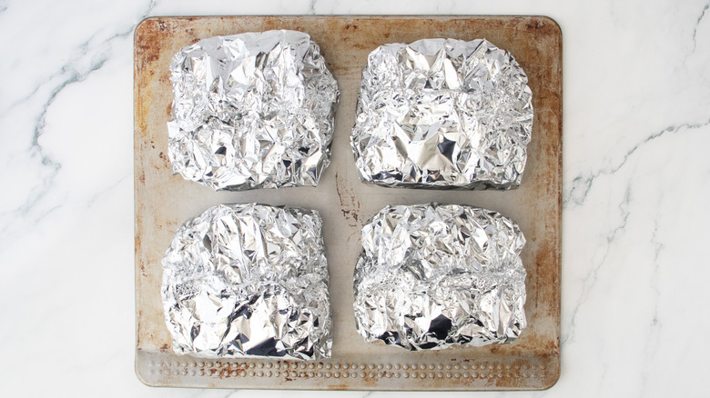 Quatre paquets de pâtes en papier d'aluminium sur une plaque à pâtisserie