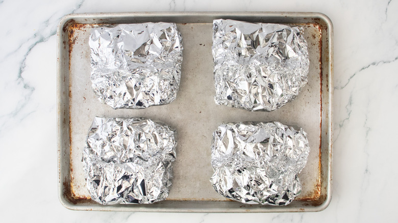 Quatre paquets de pâtes grillées dans du papier d'aluminium sur une plaque à pâtisserie