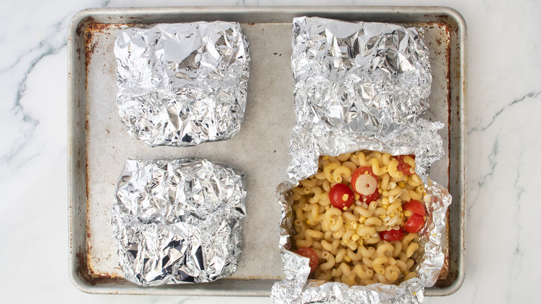 Quatre paquets de pâtes grillées dans du papier d'aluminium sur une plaque à pâtisserie, l'un est ouvert